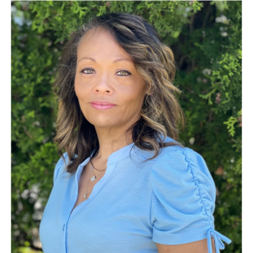 A woman in blue shirt standing next to trees.