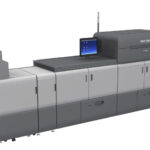 A computer printer is shown next to a large machine.
